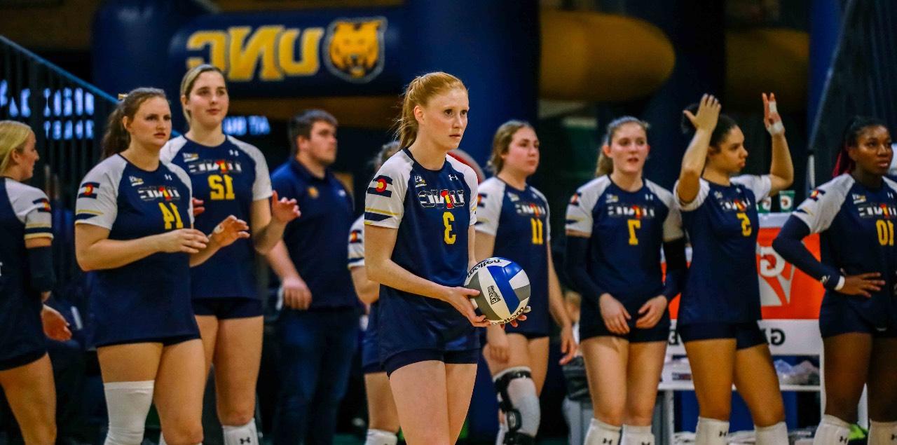 Syd Cole st和s with a volleyball in her h和s while a row of her teammates st和 behind her.